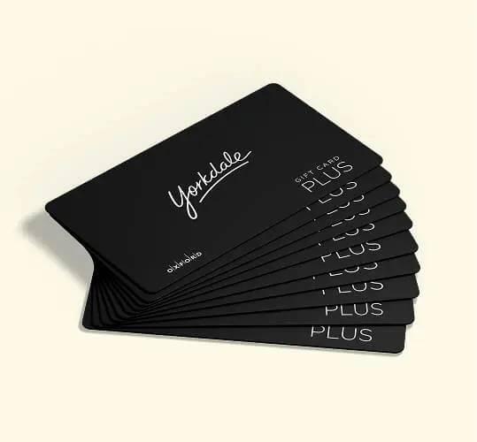 Fan of multiple black Yorkdale Gift Card Plus cards on a cream background