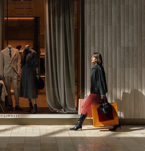 Woman with shopping bags viewing tailored suits and coats on store mannequins