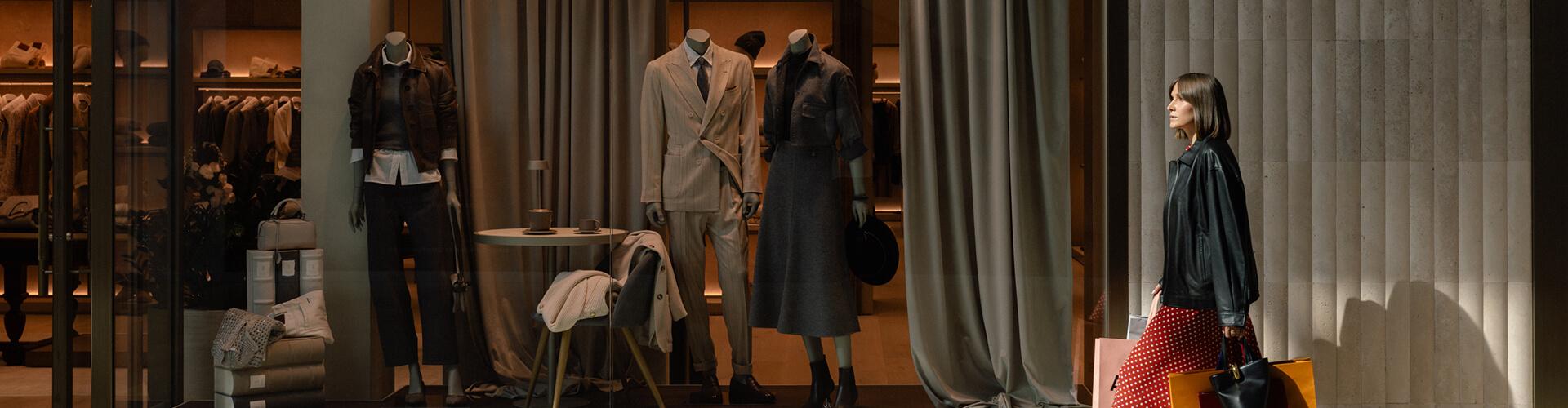 Woman with shopping bags viewing tailored suits and coats on store mannequins
