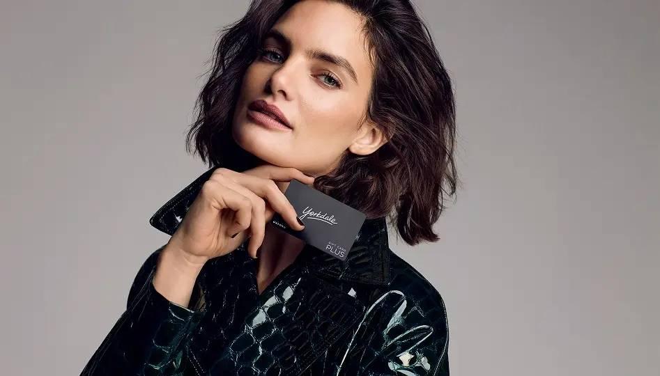 Women holding a black Yorkdale gift card while wearing a glossy black jacket