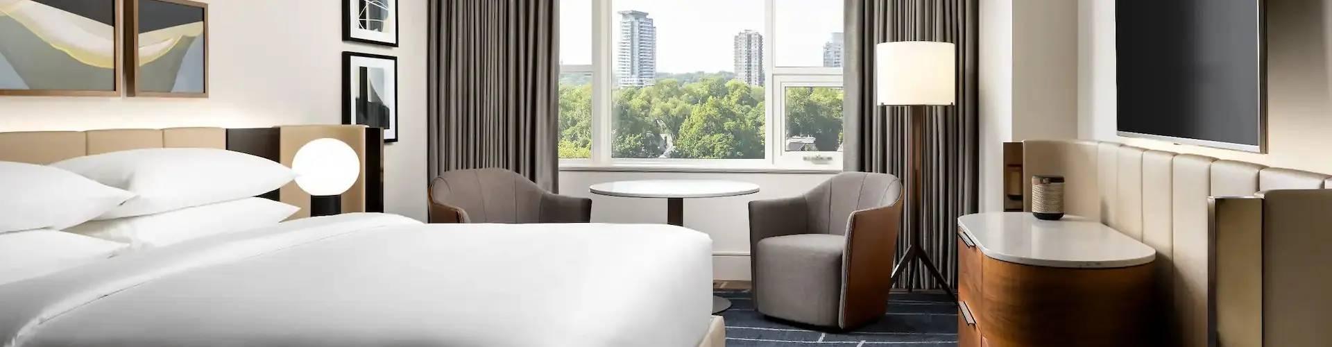Elegant hotel room with king bed, seating area, and tree views through large windows