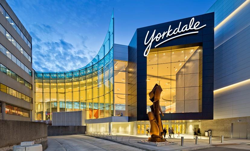 Yorkdale Shopping Centre entrance at dusk with illuminated sign and bronze sculpture