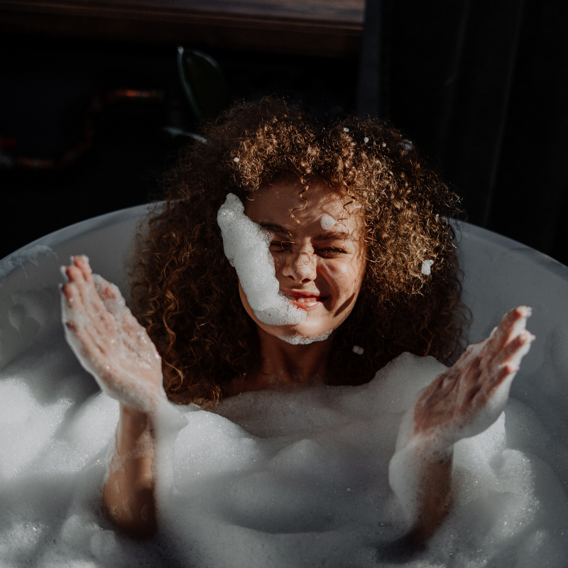 Woman with curly hair playing with bubbles in bathtub
