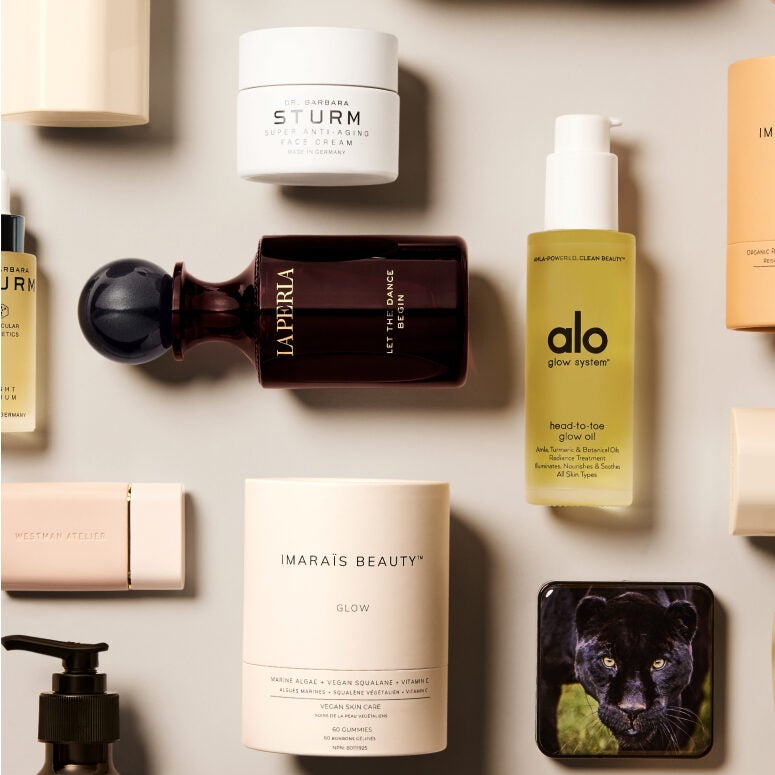 Flat lay image of a selection of various clean beauty products including Ao glow oil, Dr. Barbara Sturm face cream, La Perla perfume, and Imarais Beauty Glow serum.