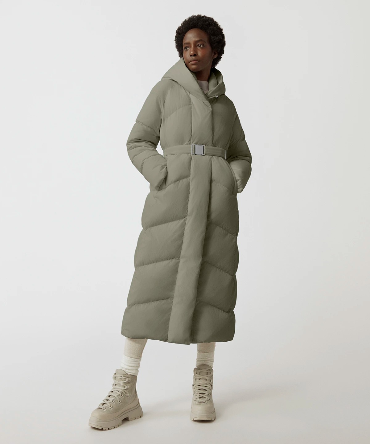 Image of a model wearing a Canada Goose Marlow parka. The parka is long with chevron quilting pattern in a sage hue.