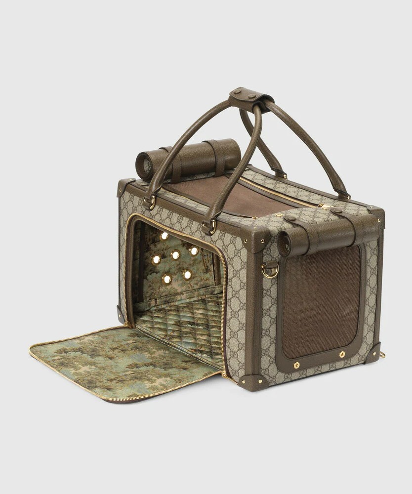 Gucci pet carrier in beige and ebony GG Supreme canvas with the historic Web colours. It features brown leather trim, a front flap opening, and a back flap with mesh window underneath.