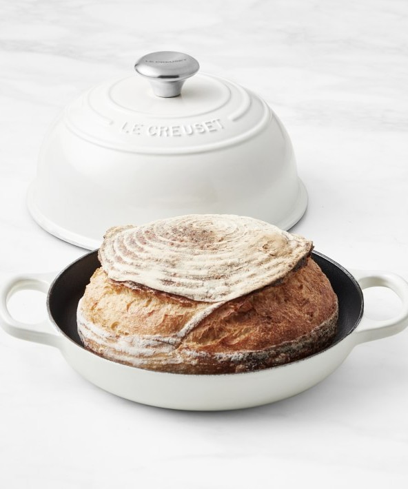 Image of a white Le Creuset Enameled Cast Iron Bread Oven with freshly baked bread inside of it.