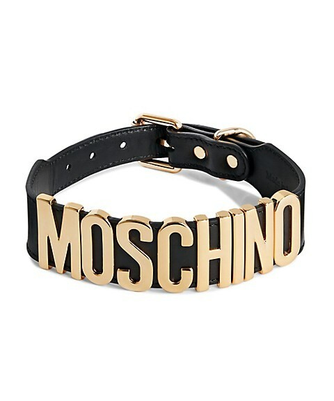 Moschino pet collar made of black leather and adorned with gold-tone lettering spelling out "MOSCHINO". The collar features a gold-[tone buckle and D-ring for attaching a leash.