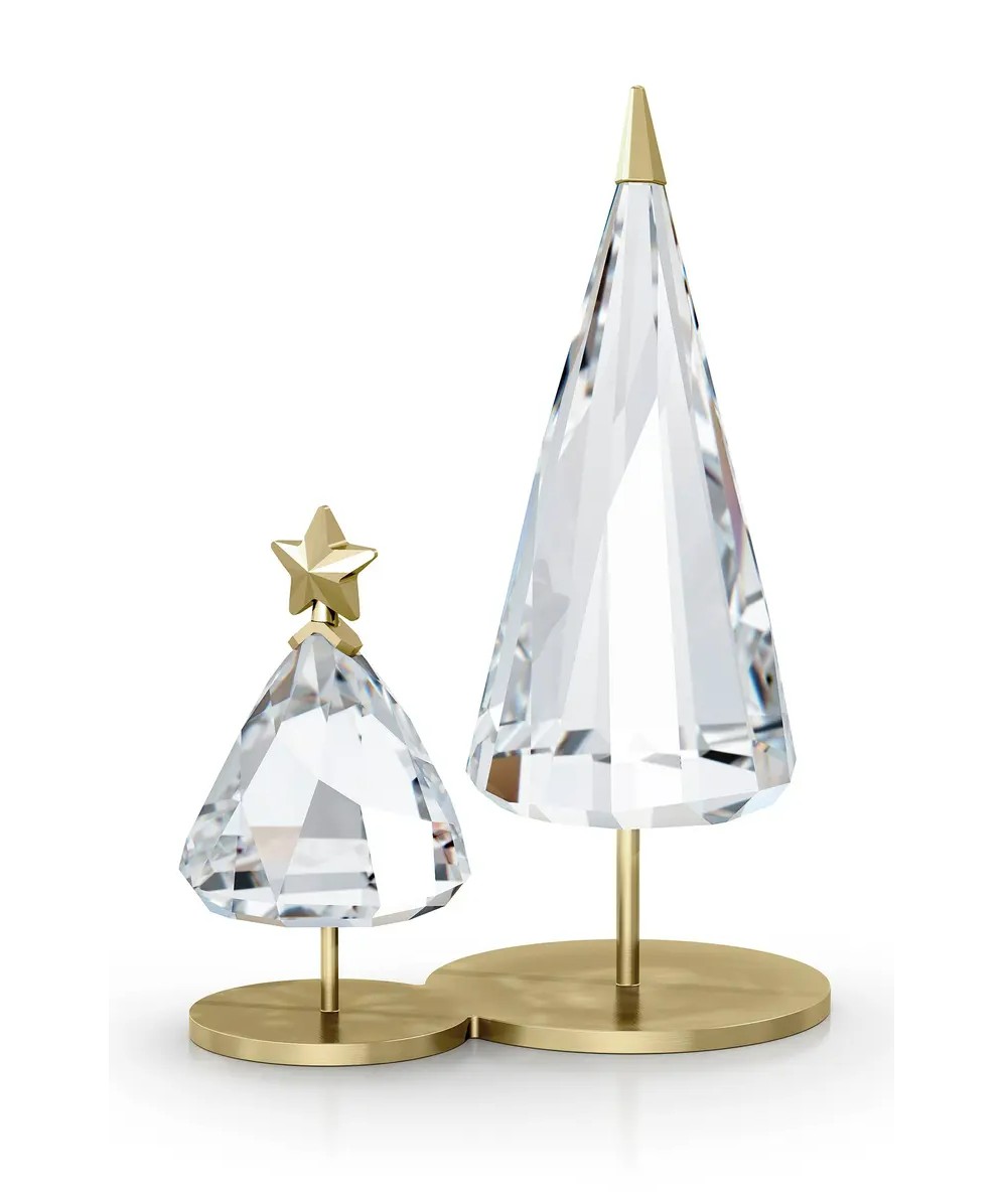 Two Swarovski Crystal Christmas trees with gold base and tree toppers. The trees are positioned on a white platform with a blurred background.