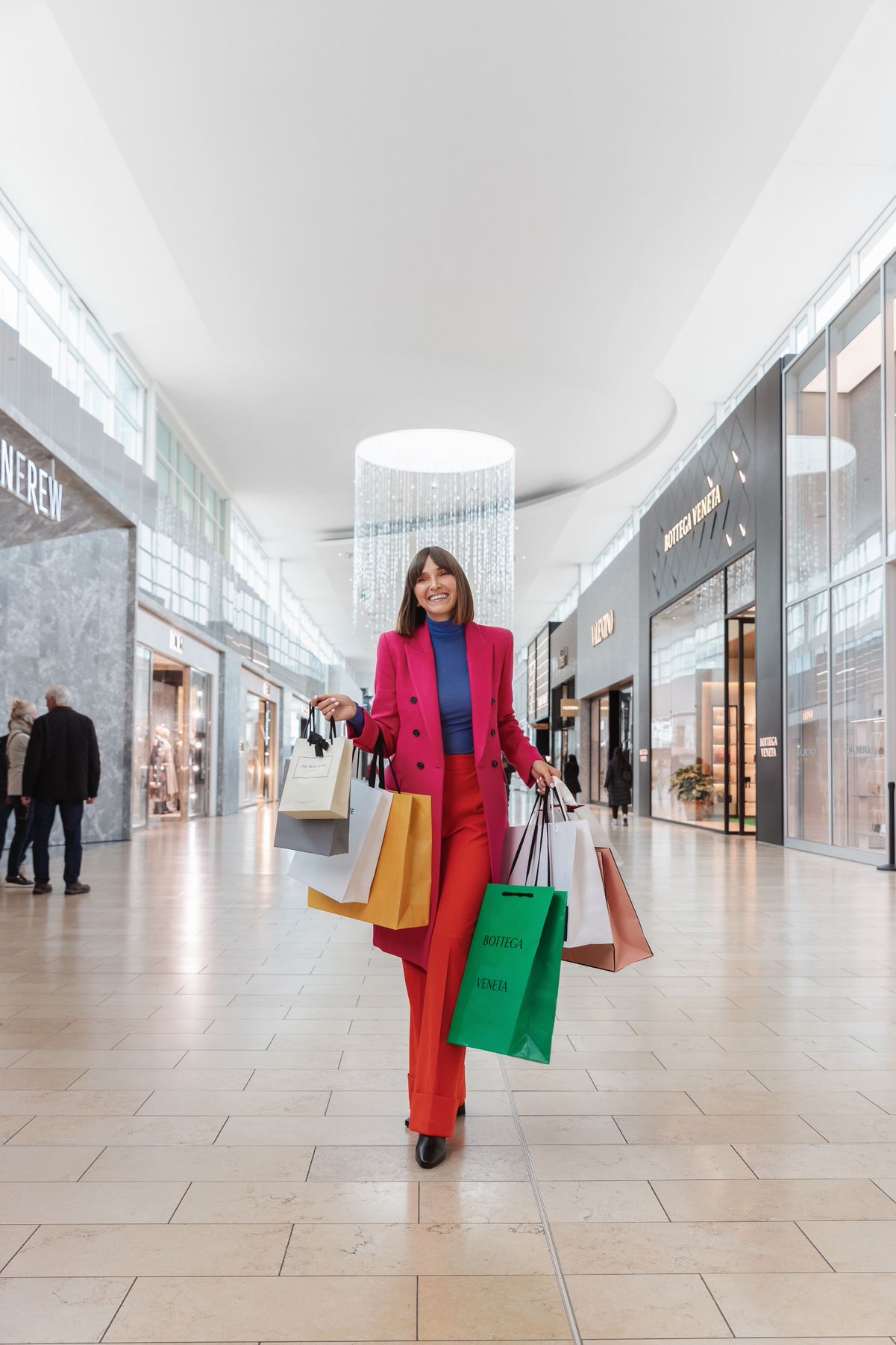 Image of a woman wearing a colourful outfit shopping at Yorkdale shopping centre. She holds several shopping bags and is smiling.
