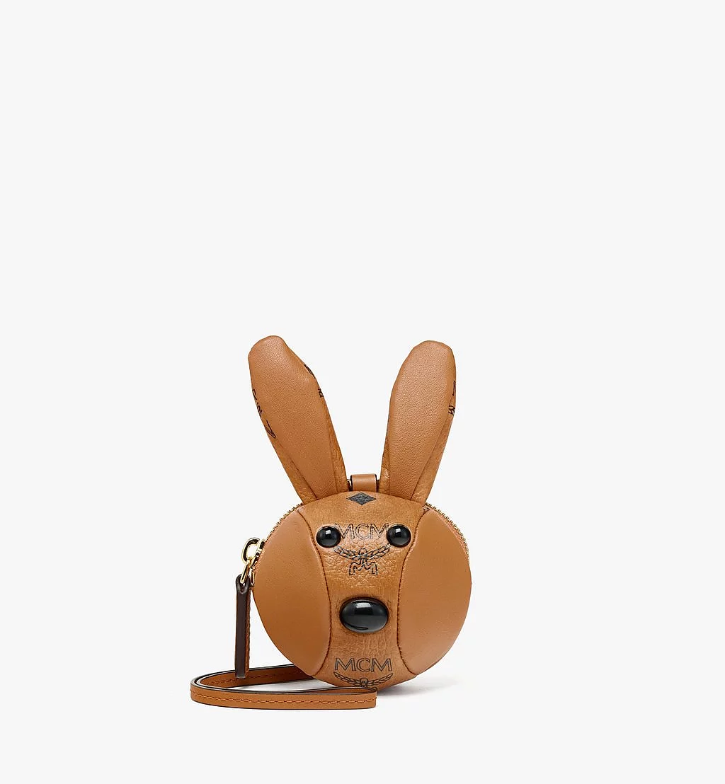 Image of a small MCM charm in the shape of a bunny head. It's made of leather and features the MCM logo print.