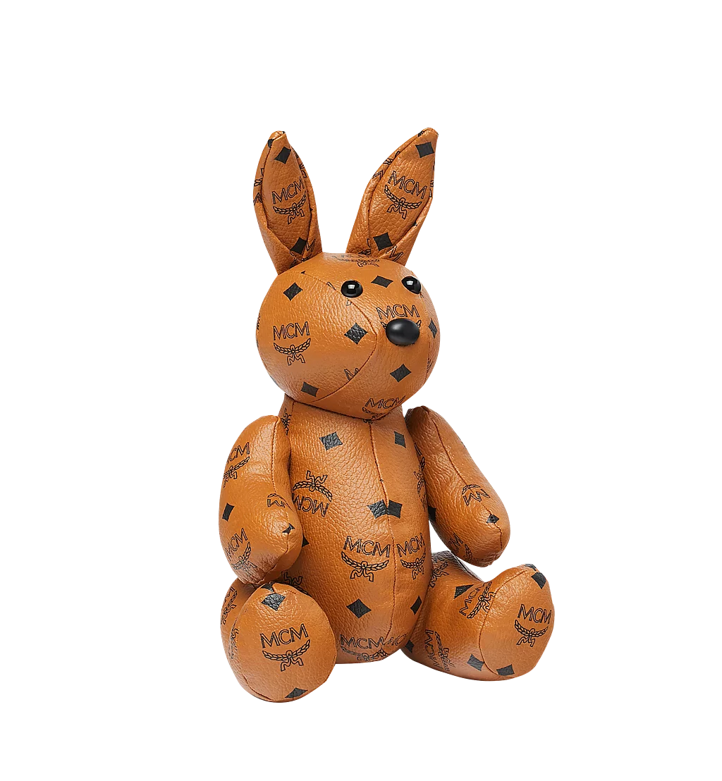 Image of an MCM stuffed animal in the shape of a bunny. The fabric is leather and features the MCM logo print.