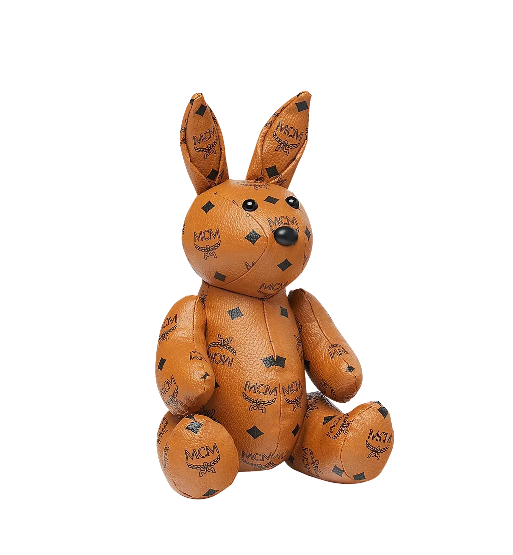 Image of an MCM stuffed animal in the shape of a bunny. The fabric is leather and features the MCM logo print.