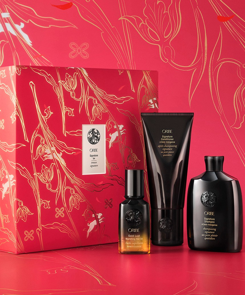Product image of Oribe Lunar New Year gift set. There is a large red and gold gift box and three glossy black bottles of Oribe hair products beside it.