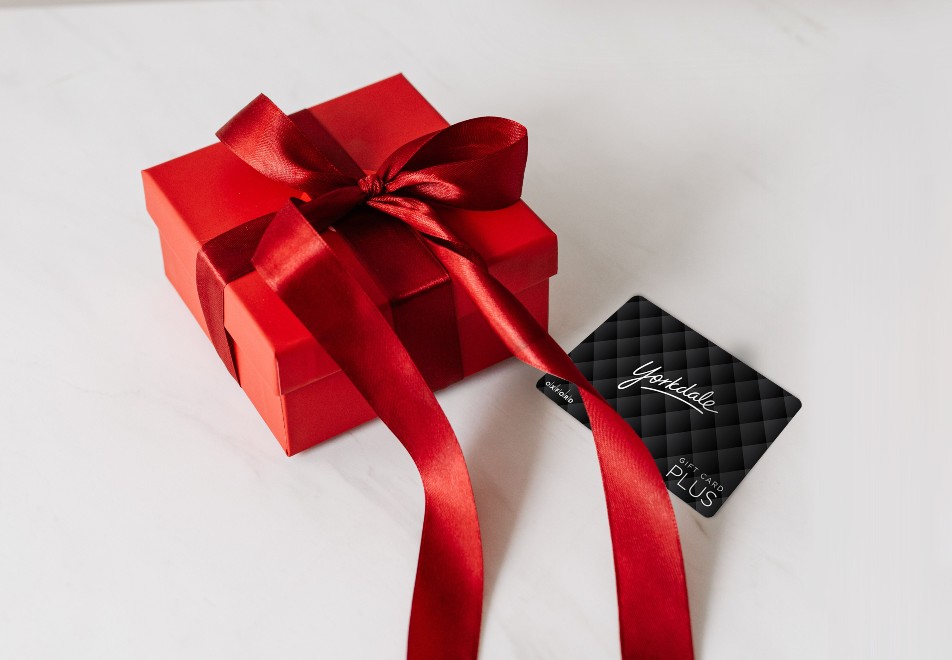 Image of a red gift box with a red bow on a white backdrop. Beside it is a black Yorkdale gift card