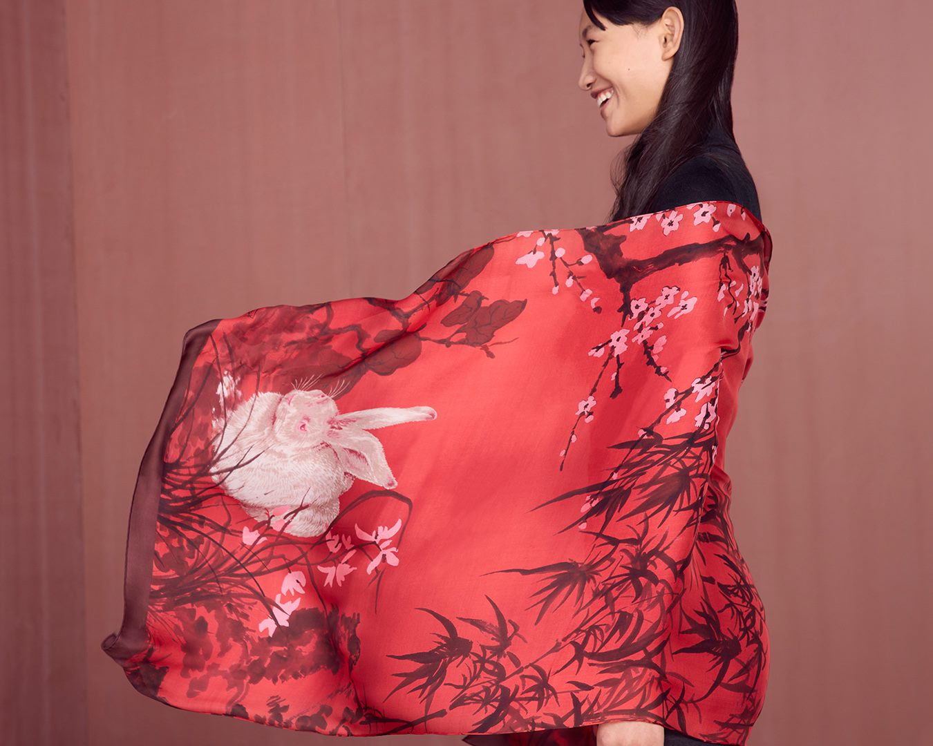 Profile image of a model holding out a large, red Ferragamo silk scarf featuring cherry blossoms, trees and a bunny.