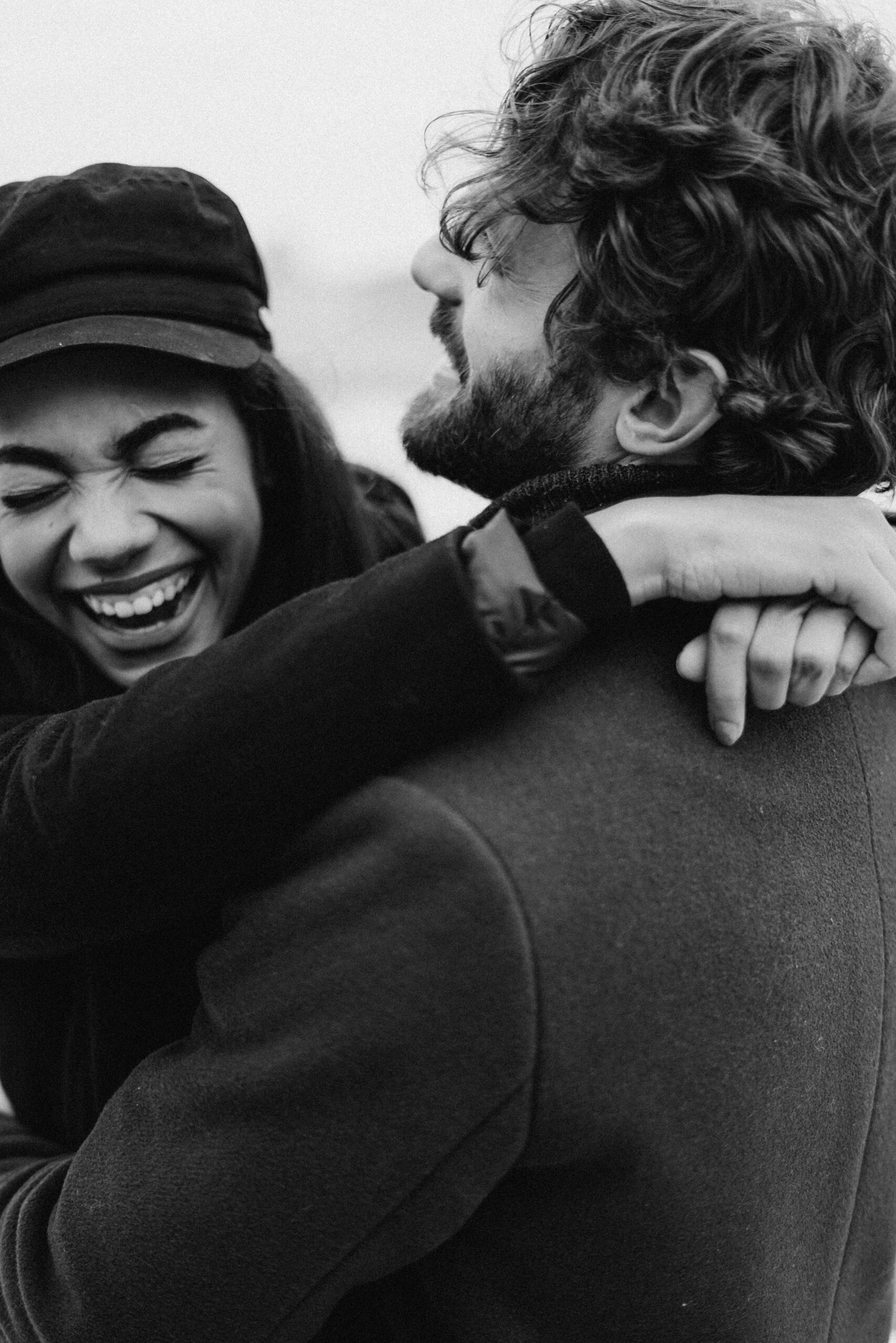 Black and white image of a couple with their arms around each other, laughing.
