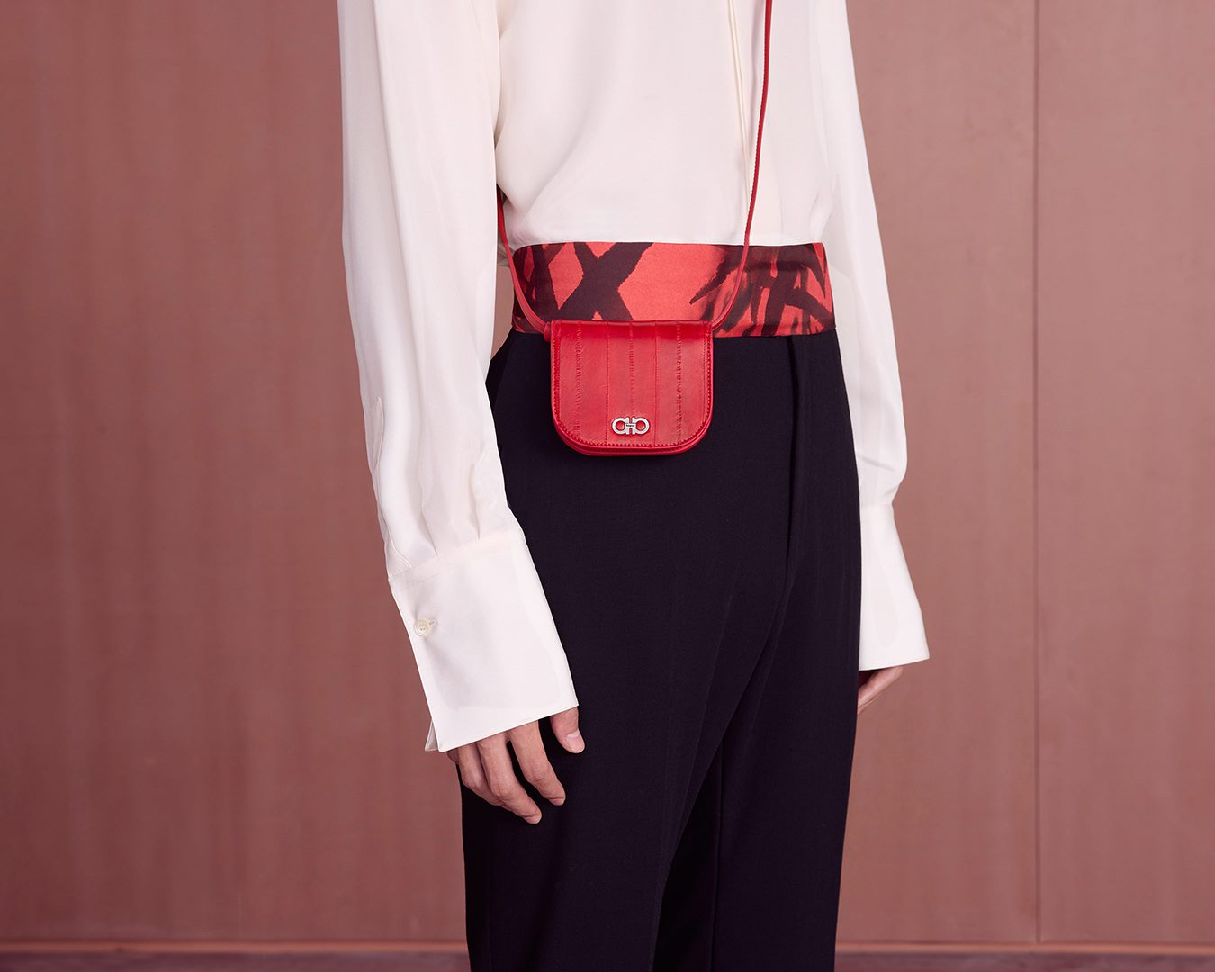 Image of a model wearing a silk white dress shirt, black trousers and a red silk Ferragamo thin scarf tied around her waist. She also wears a small, red Ferragamo cross body bag.