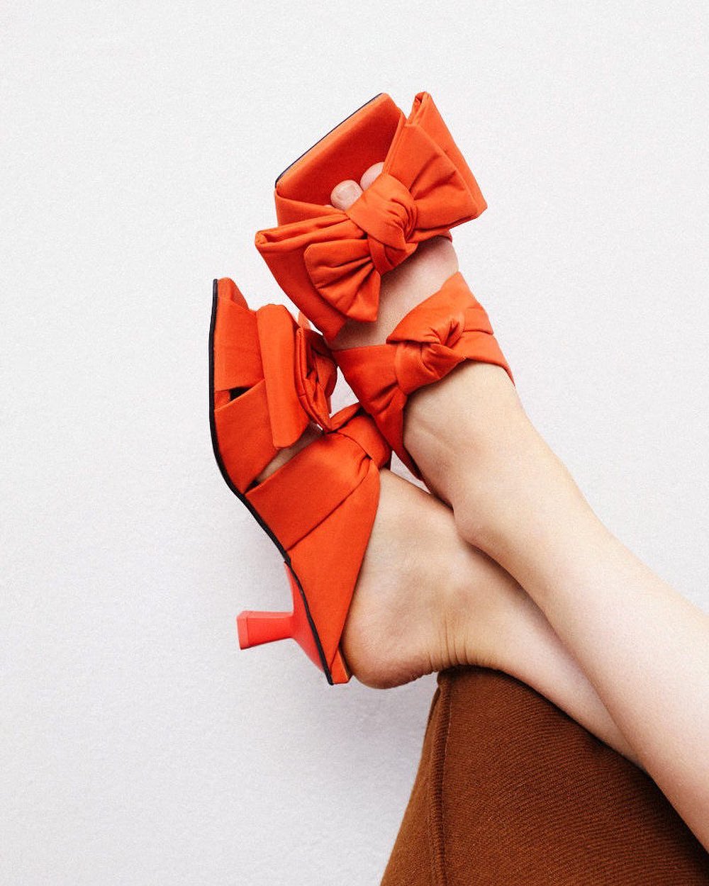 Model wearing bright orange GANNI kitten heels with two bows.