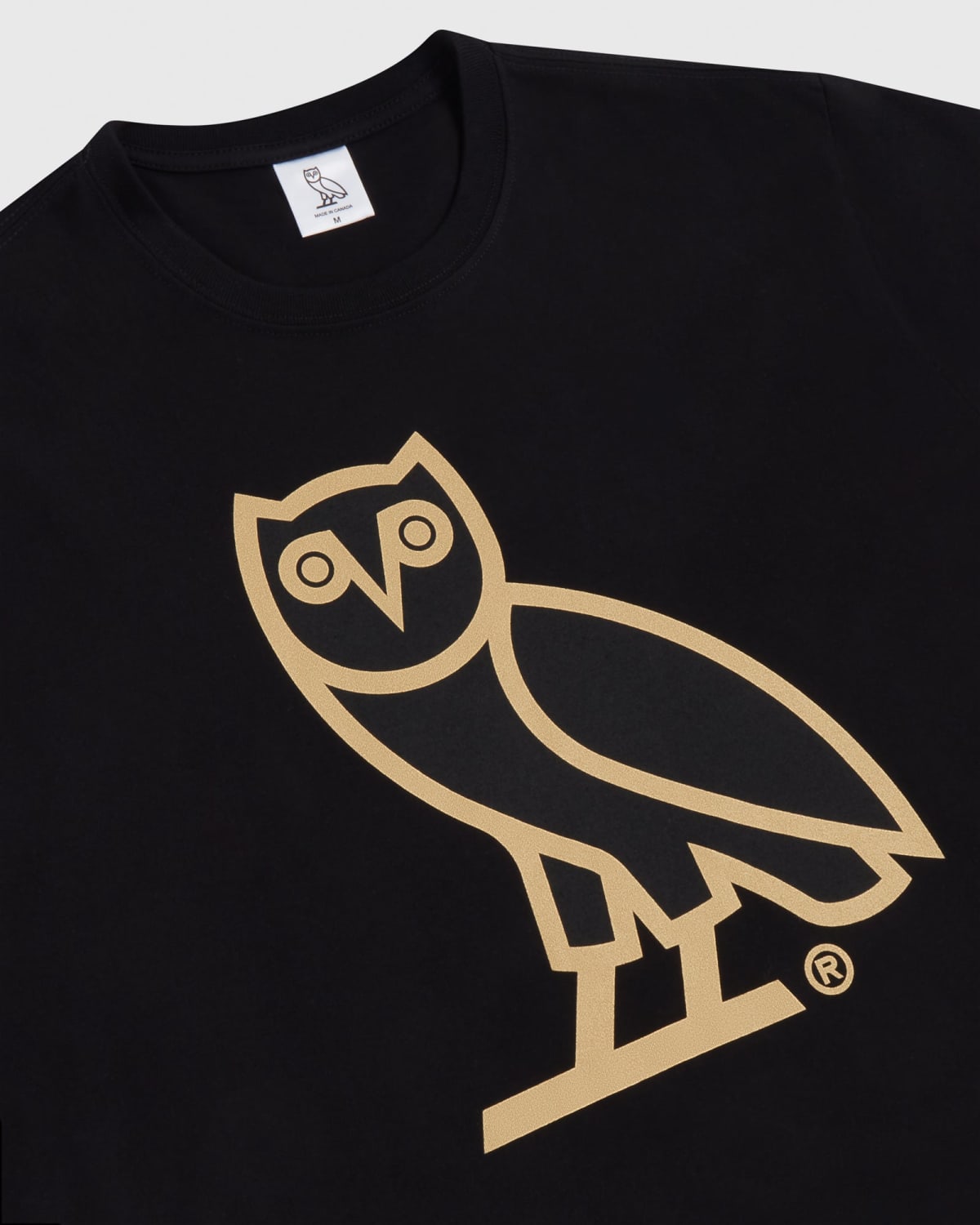 A close-up image of a black OVO crewneck sweater with a gold outline of an owl on the front