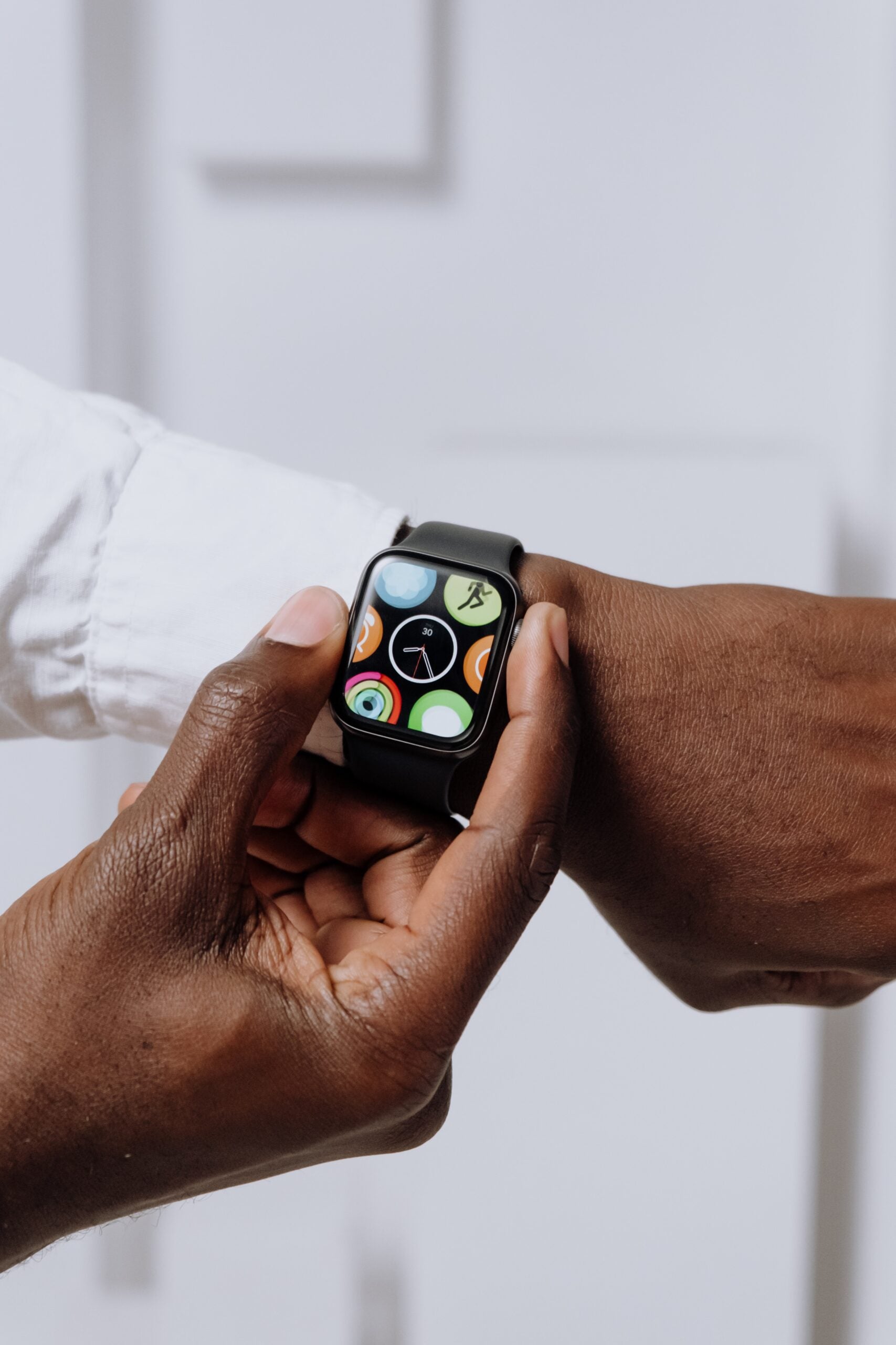 Close up image of an Apple watch on a person's left wrist. The cuff of a white dress shirt is visible. The person's right hand is adjusting the watch.