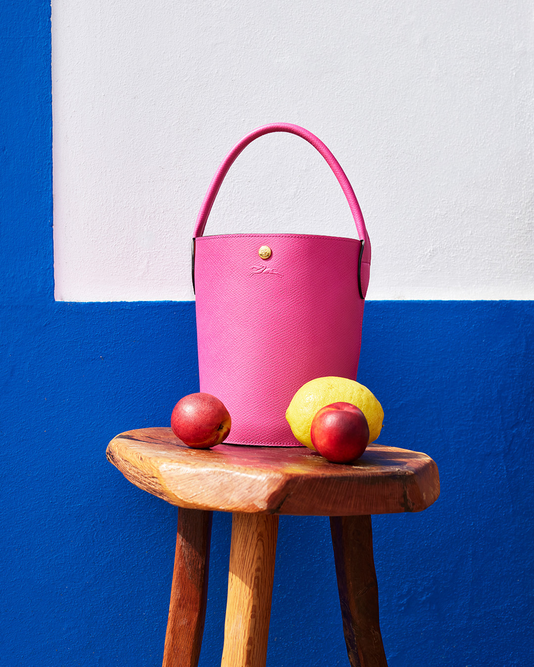 image of a pink longchamp bucket bag perched atop a wooden stool with fruits surrounding it.