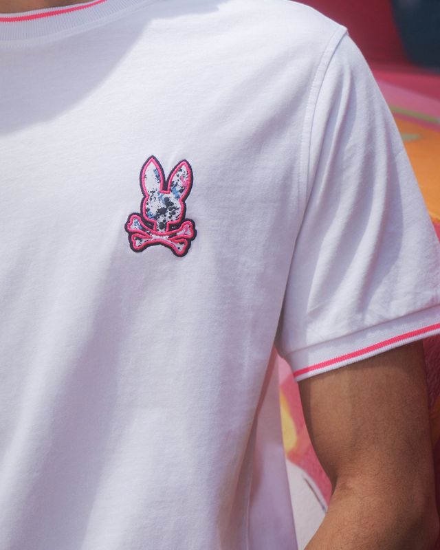 close-up image of a model wearing a white t-shirt with psycho bunny's logo on the left chest
