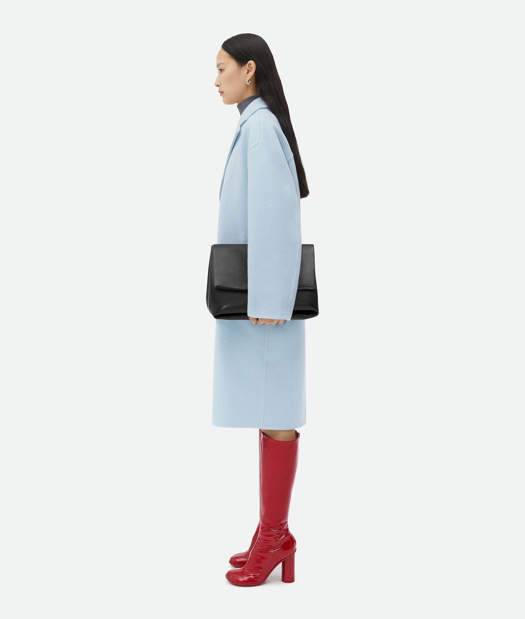 Black Bottega Veneta Purse on a model with a light blue pea coat and red boots. Shop at the Centre of Style, Yorkdale Shopping Centre.