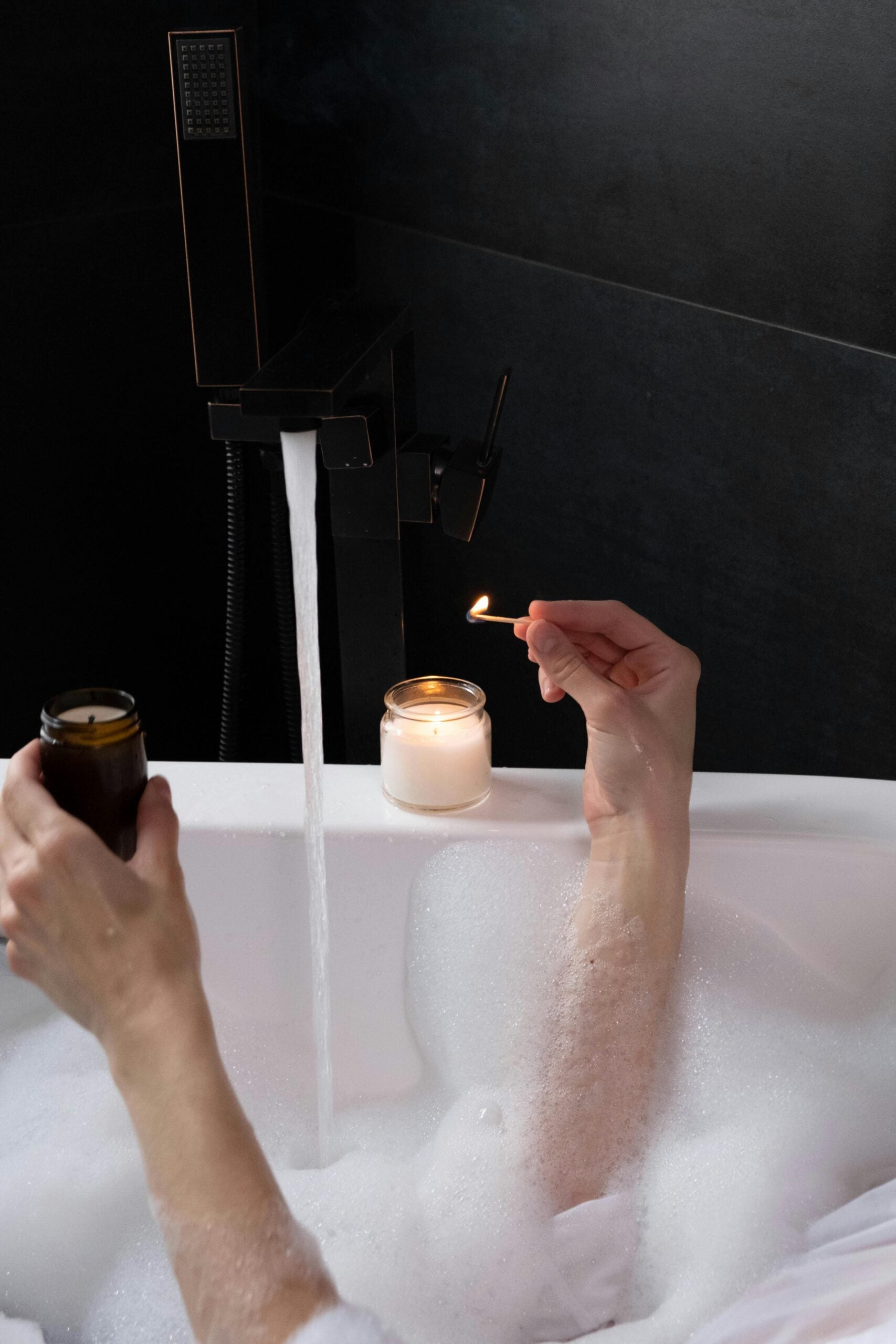 Person lighting a candle in a bubble bath